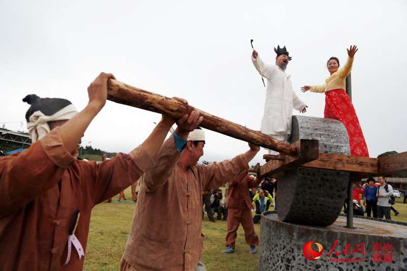 民俗節上，兩名身著華麗服裝的人站在“石磨”上載歌載舞