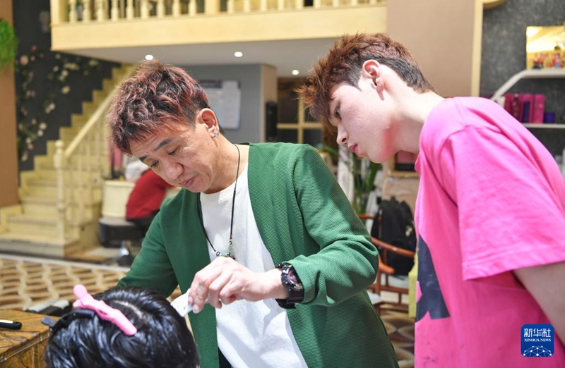 在位于烏魯木齊市城區的美發店，安鐘旭（左）為一名顧客理發，實習生達爾汗·居瑪別克在一旁觀察學習（3月15日攝）。達爾汗來自新疆尼勒克縣牧民家庭，想開一家理發店，經朋友介紹，從2024年開始跟著安鐘旭學習。